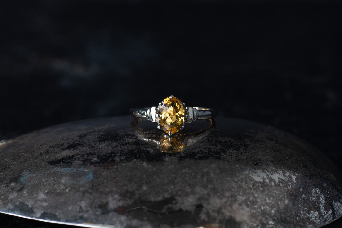 Vintage style ring featuring a claw set oval citrine solitaire on a dark reflective surface.