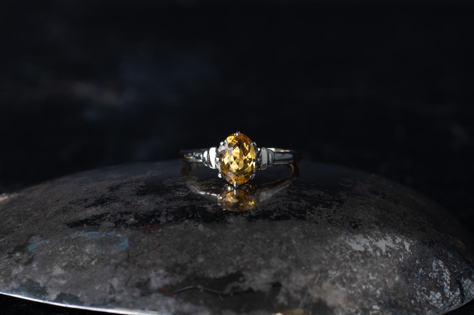 Vintage style ring featuring a claw set oval citrine solitaire on a dark reflective surface.