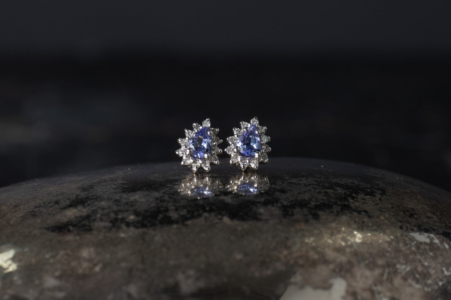 Pair of 9ct white gold stud earrings featuring pear cut tanzanites surrounded by a diamond halo cluster.