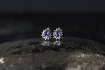 Pair of 9ct white gold stud earrings featuring pear cut tanzanites surrounded by a diamond halo cluster.
