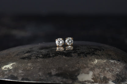Pair of 9ct yellow gold stud earrings featuring brilliant cut diamonds claw set on a dark reflective surface.