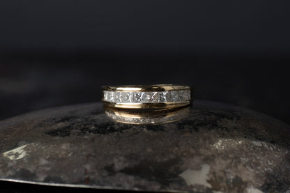 18ct yellow gold half eternity ring featuring a row of princess cut diamonds channel set between smooth gold rails.