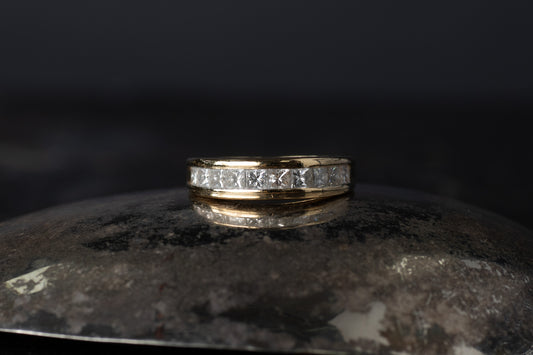 18ct yellow gold half eternity ring featuring a row of princess cut diamonds channel set between smooth gold rails.