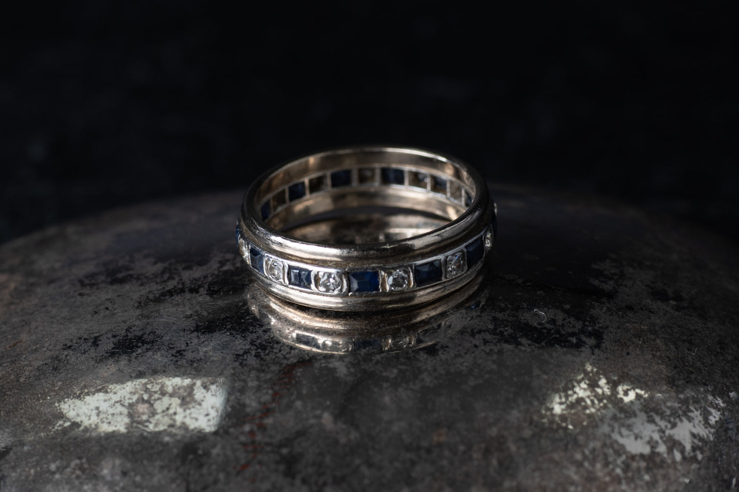Antique platinum full eternity ring featuring alternating square blue sapphires and round diamonds set around the entire band.