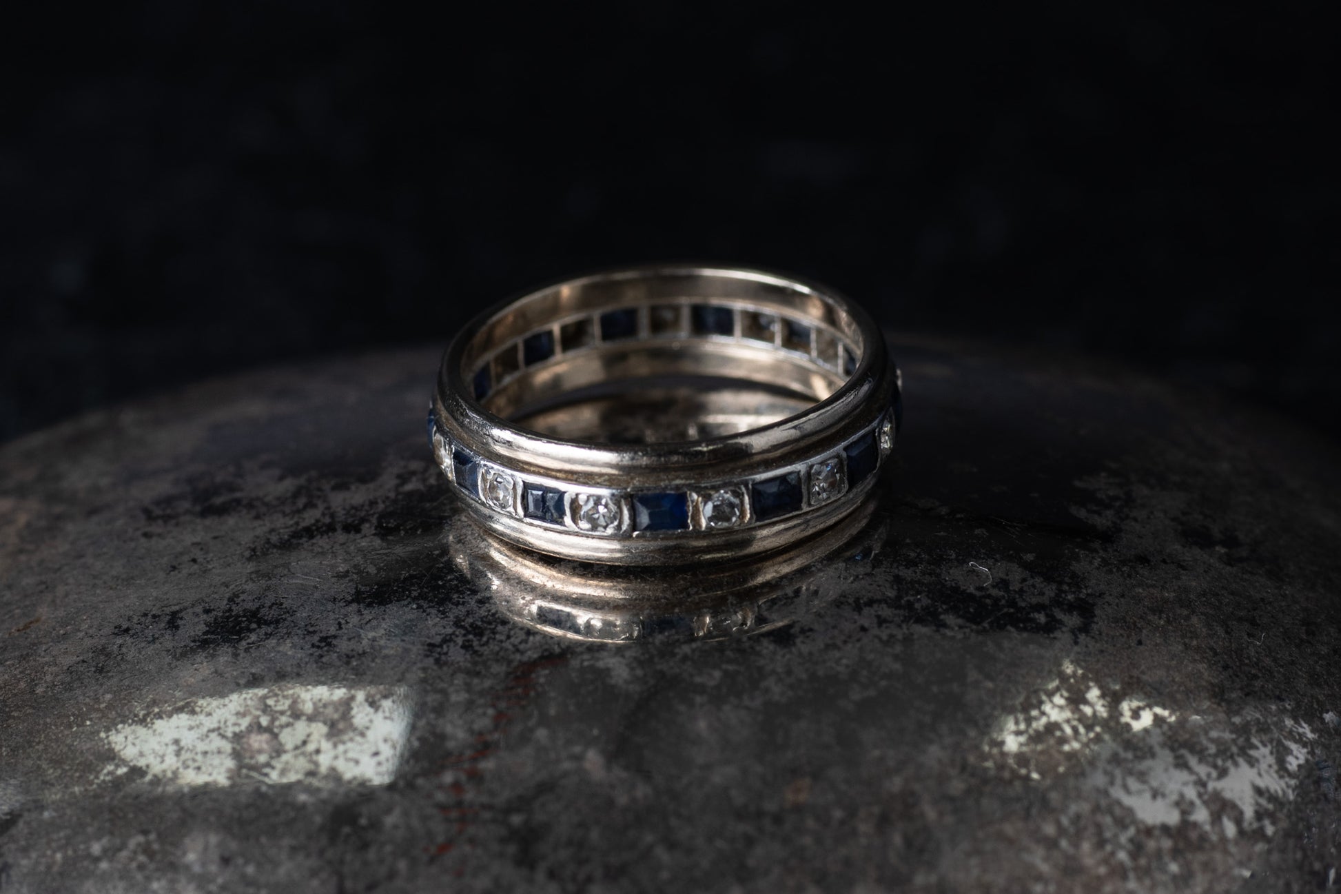 Antique platinum full eternity ring featuring alternating square blue sapphires and round diamonds set around the entire band.