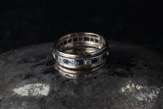 Antique platinum full eternity ring featuring alternating square blue sapphires and round diamonds set around the entire band.