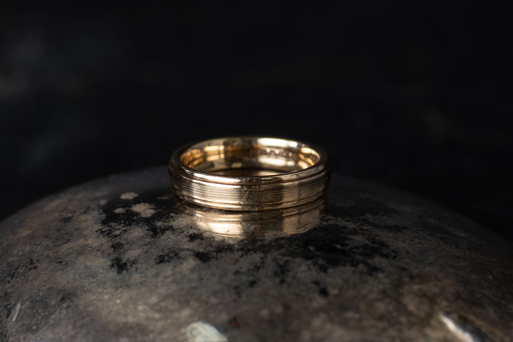 9ct yellow gold wedding band featuring a horizontal ribbed texture design resting on a dark reflective surface.