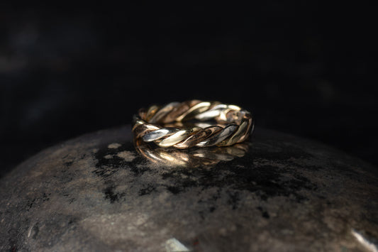 9ct gold ring featuring intertwined bands of yellow, white, and rose gold in a twist design on a dark reflective surface.