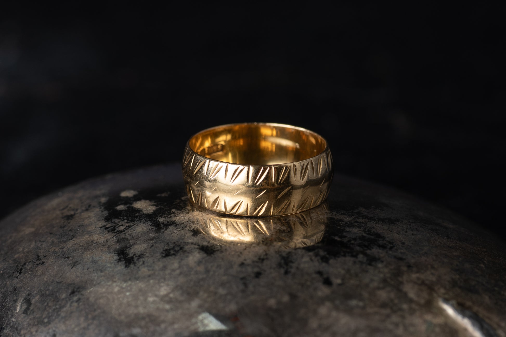 Close up of 18ct yellow gold wide band ring with etched diagonal pattern on dark stone.