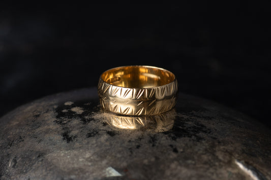 Close up of 18ct yellow gold wide band ring with etched diagonal pattern on dark stone.