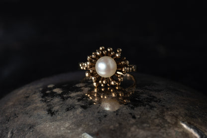 Front view of 9ct yellow gold pearl solitaire ring with textured starburst halo on dark background.