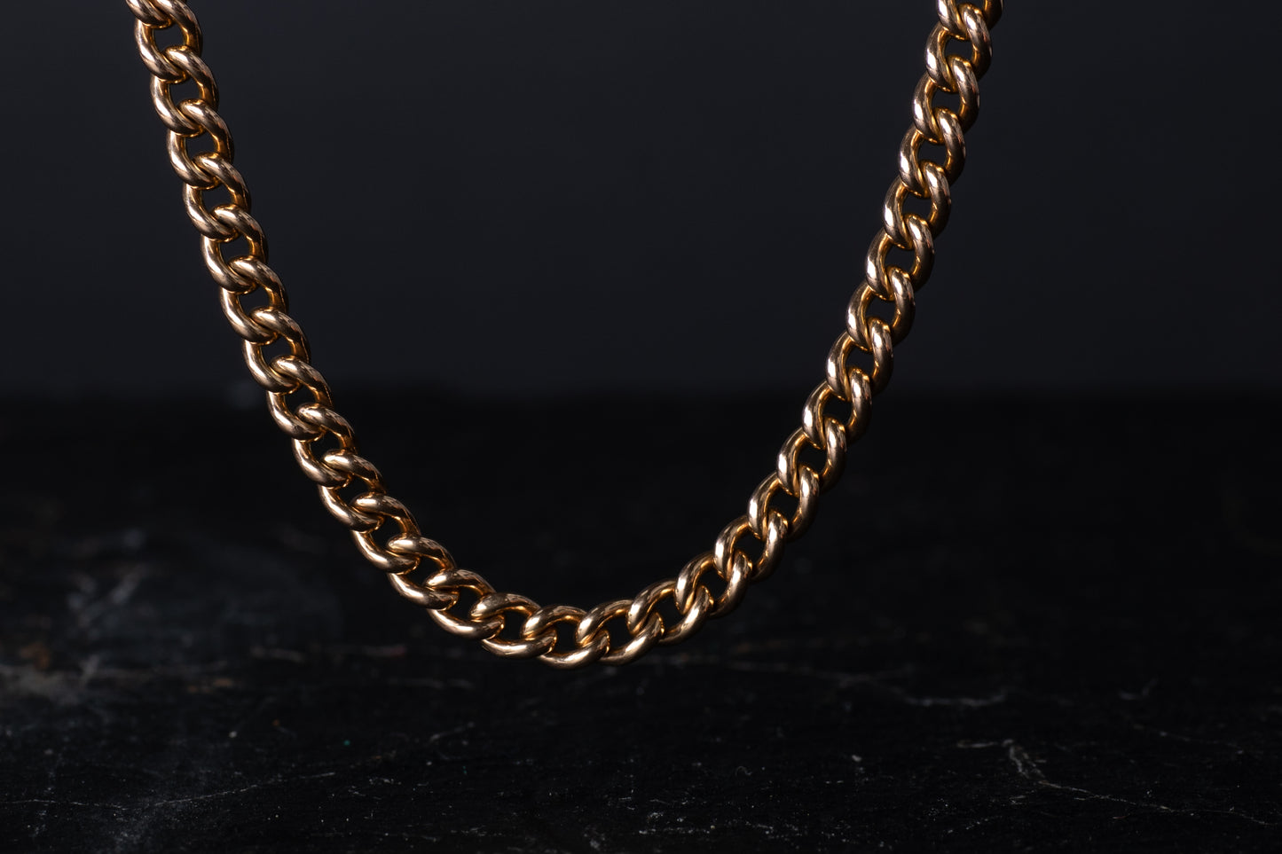 Front view of solid 9ct rose gold curb link Albert chain necklace draping against a dark background.