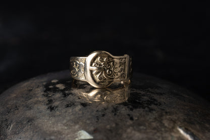 Close up of vintage 9ct yellow gold ring with belt buckle design and engraved scrollwork on dark background.