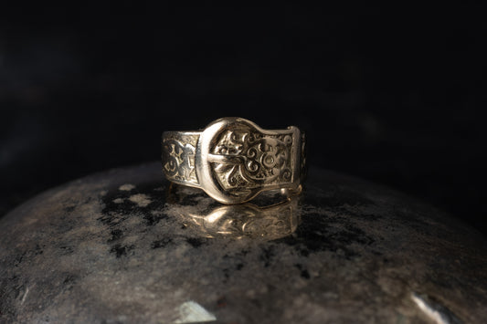 Close up of vintage 9ct yellow gold ring with belt buckle design and engraved scrollwork on dark background.