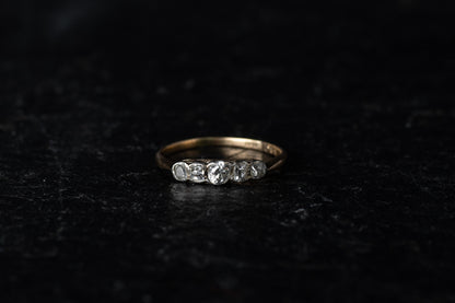Front view of antique five stone diamond ring with platinum rub over setting on a yellow gold band against a dark textured background.