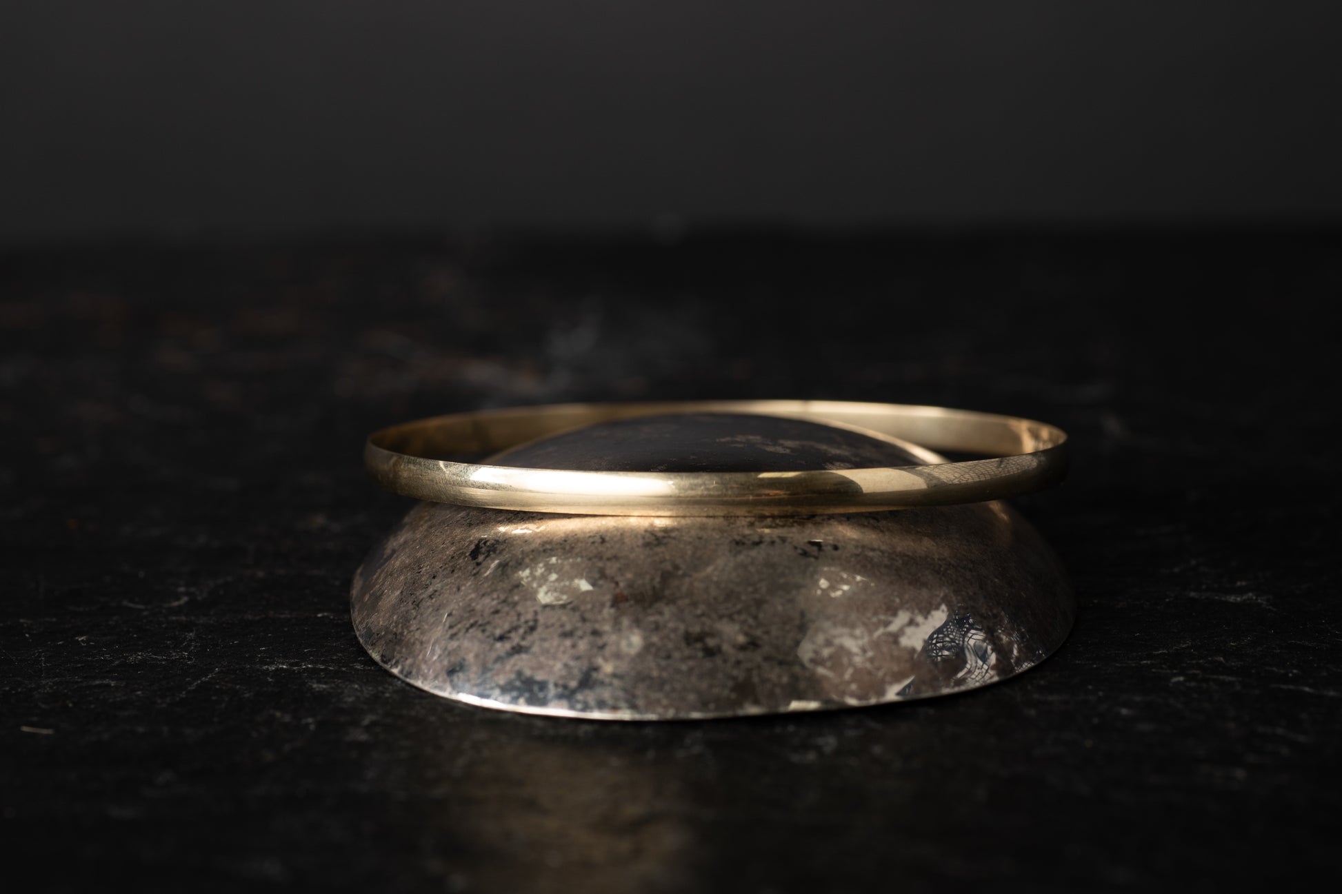 Eye-level view of 9ct yellow gold round bangle showcasing smooth curvature on dark stone background.