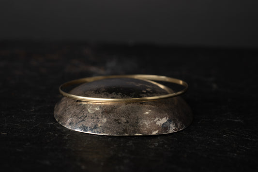 Low angle view of simple 9ct yellow gold wire bangle resting on a dark, textured stone surface.