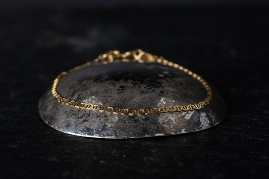 Side view of 9ct yellow gold fancy flat link bracelet with mariner-style links resting on a dark stone background.