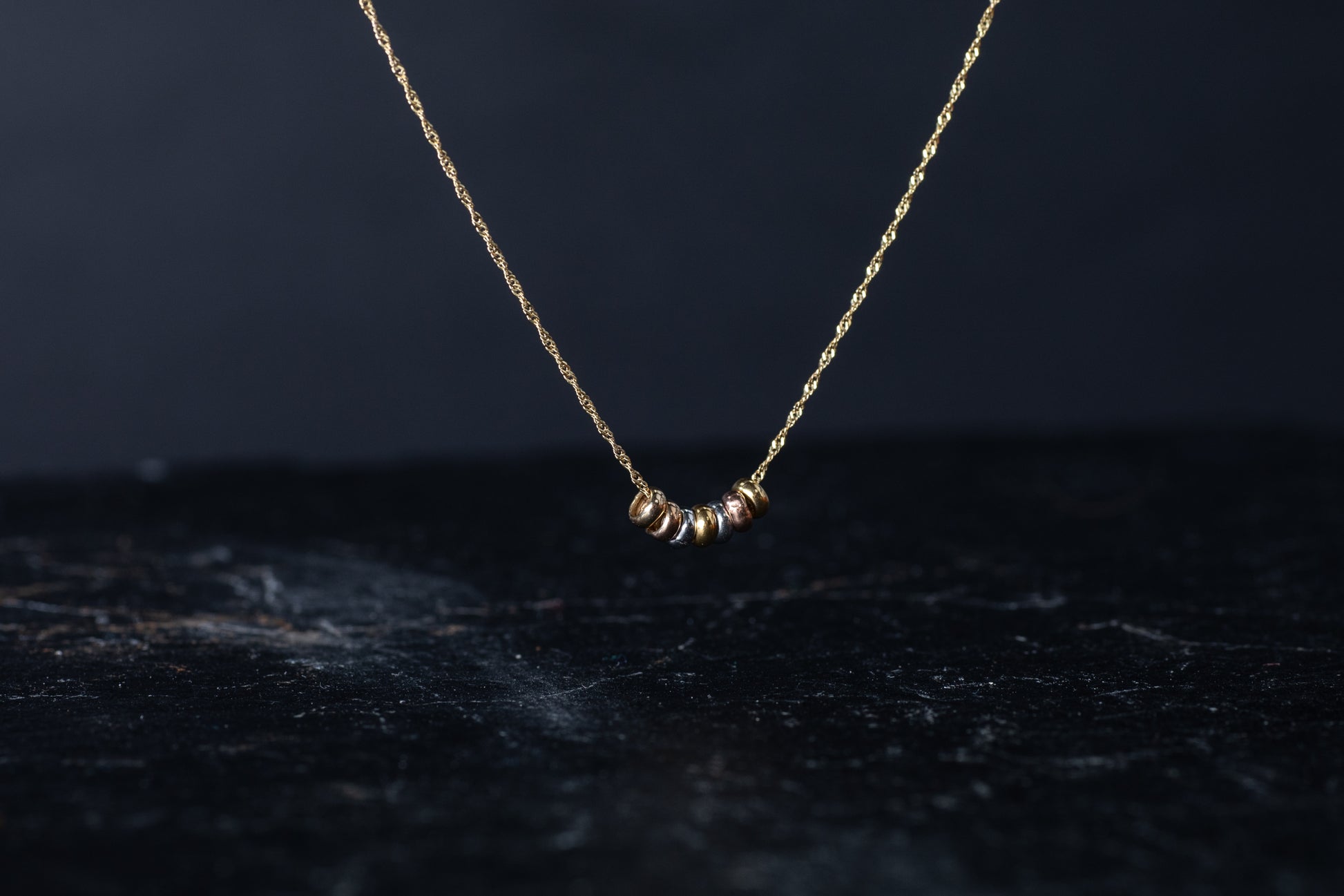 Front view of three tone gold necklace featuring seven mixed metal round slider beads on a twisted gold chain.
