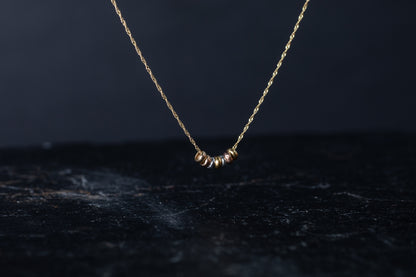 Front view of three tone gold necklace featuring seven mixed metal round slider beads on a twisted gold chain.