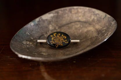 Oval pressed flower brooch with yellow florals on black background rub over set on silver bar pin.