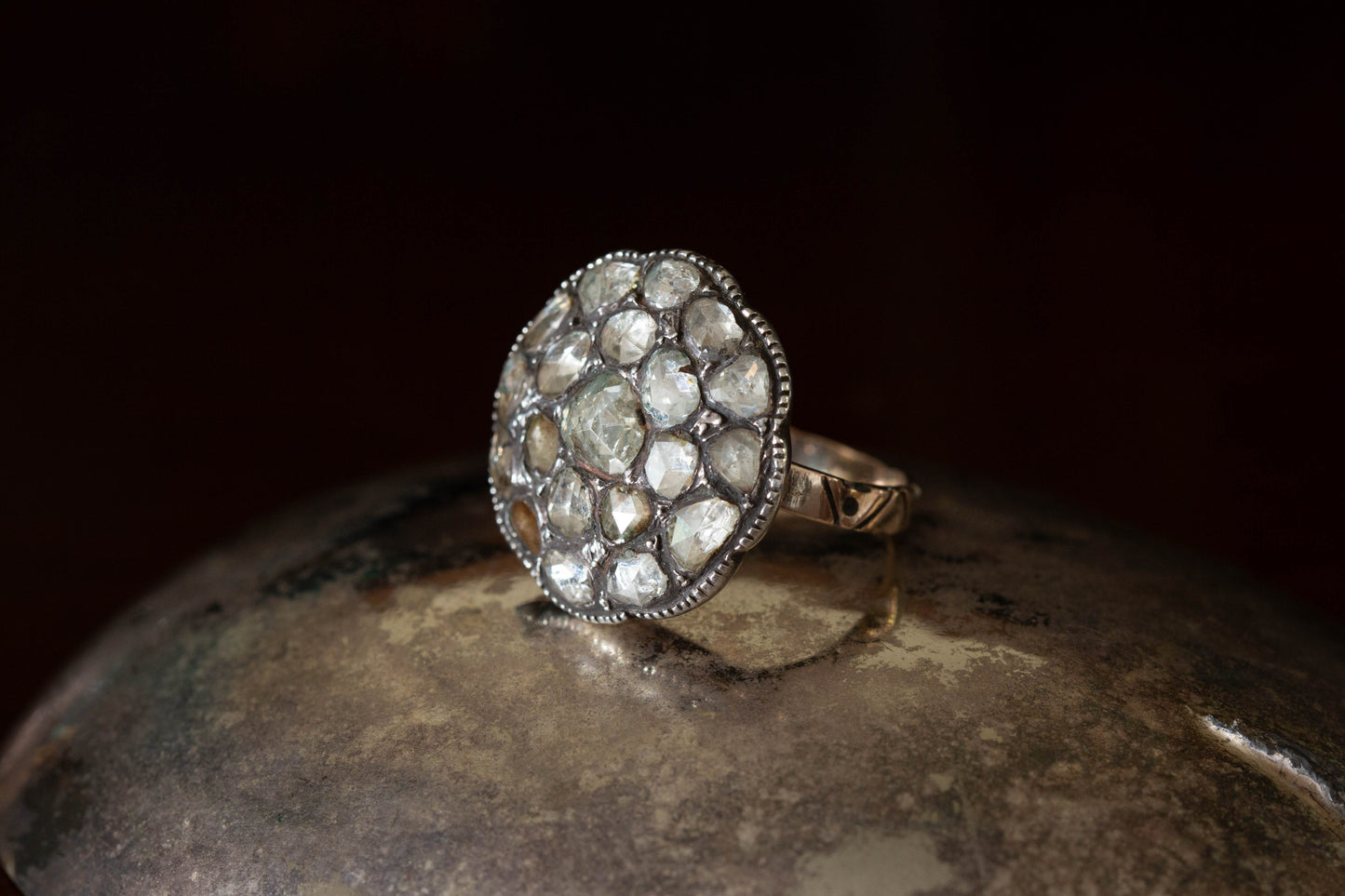 Side angle of sterling silver cluster ring featuring large circular rose cut diamonds with millegrain setting on dark prop.