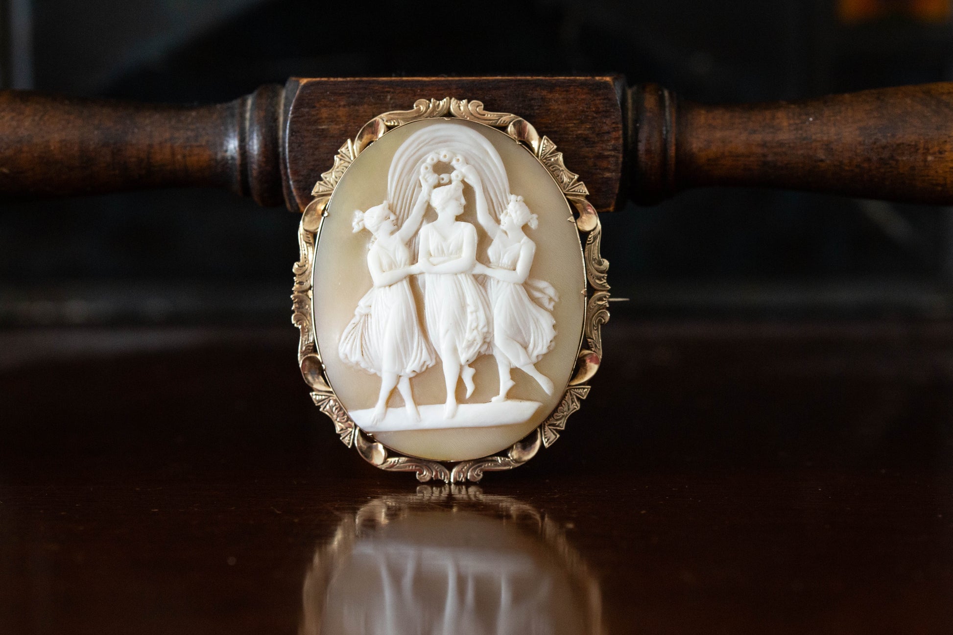 Front view of carved mother of pearl cameo brooch depicting three dancing figures in 14ct gold claw setting.