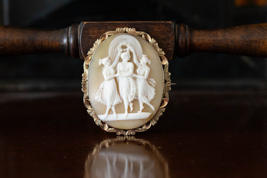 Front view of carved mother of pearl cameo brooch depicting three dancing figures in 14ct gold claw setting.