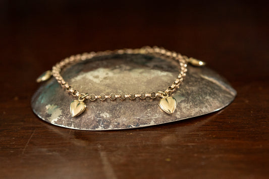 9ct rose gold belcher link bracelet featuring five evenly spaced heart charms resting on a dark stone background.