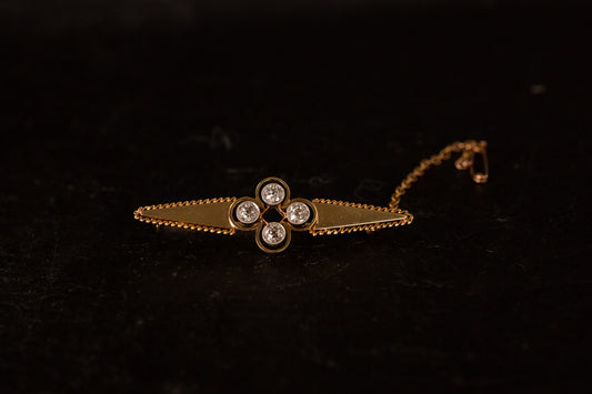 Antique 18ct yellow gold bar brooch featuring a central diamond cluster and safety chain on a dark background.
