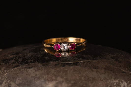Front view of antique 18ct gold ring with rubies and old mine cut diamond rub over set on dark stone.