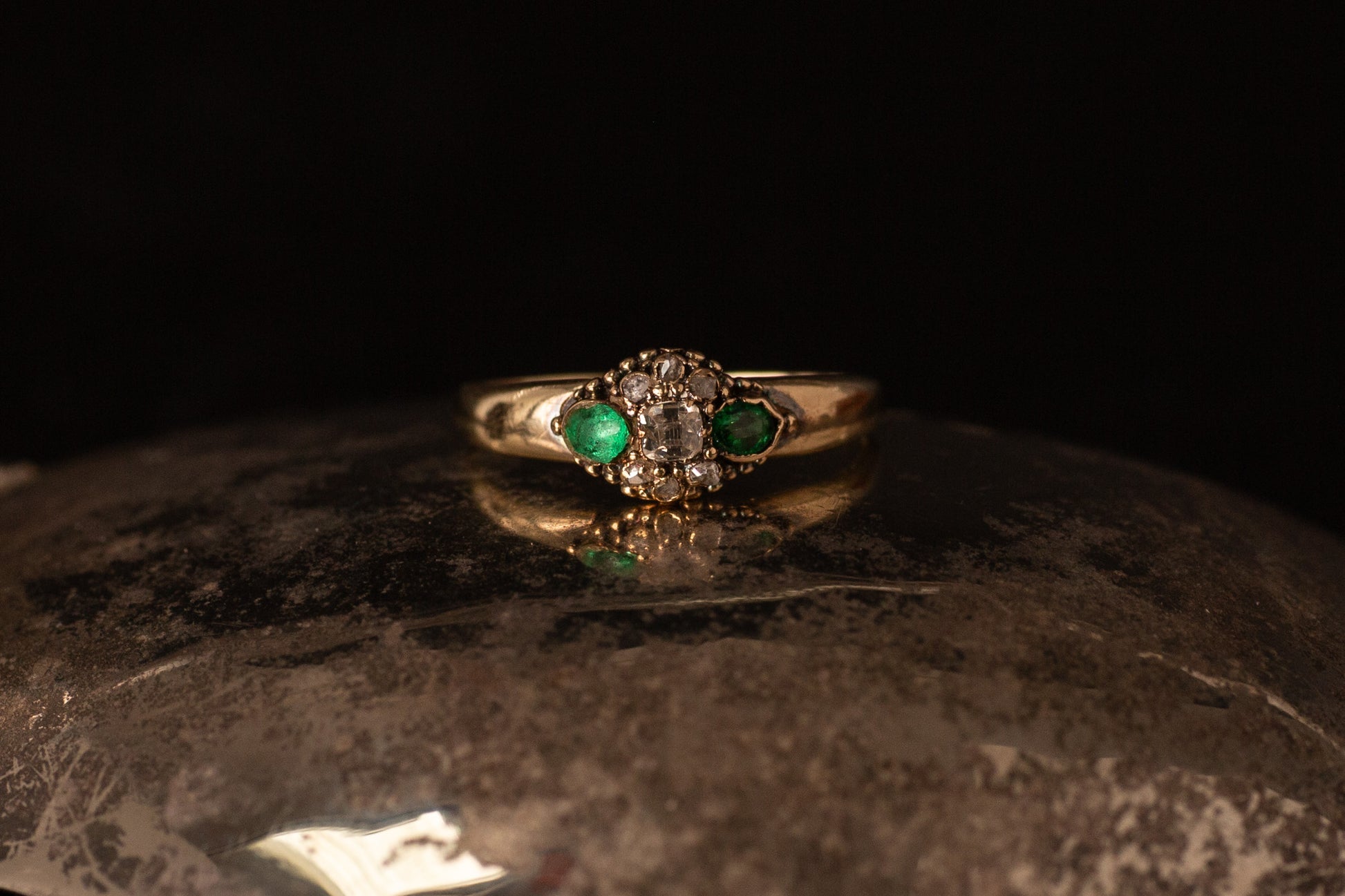 Front view of antique 14ct yellow gold ring featuring a central diamond cluster flanked by two emeralds on dark stone.