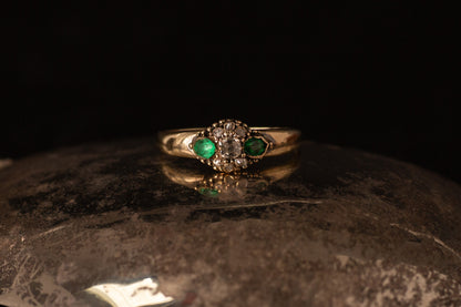 Front view of antique 14ct yellow gold ring featuring a central diamond cluster flanked by two emeralds on dark stone.