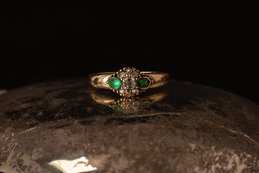 Front view of antique 14ct yellow gold ring featuring a central diamond cluster flanked by two emeralds on dark stone.