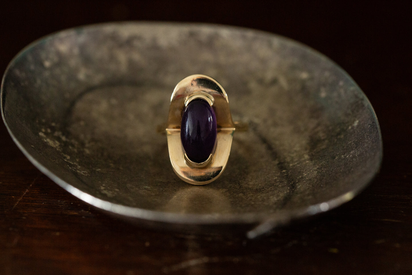 Front view of 9ct yellow gold ring with oval cabochon amethyst rub over set on dark background.