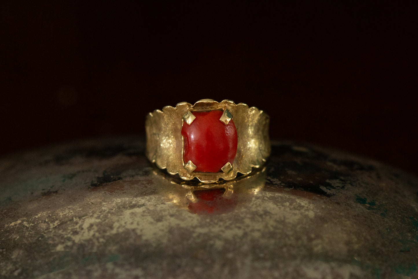 Front view of 18ct yellow gold ring featuring a square-ish red coral cabochon claw set on a wide textured band.