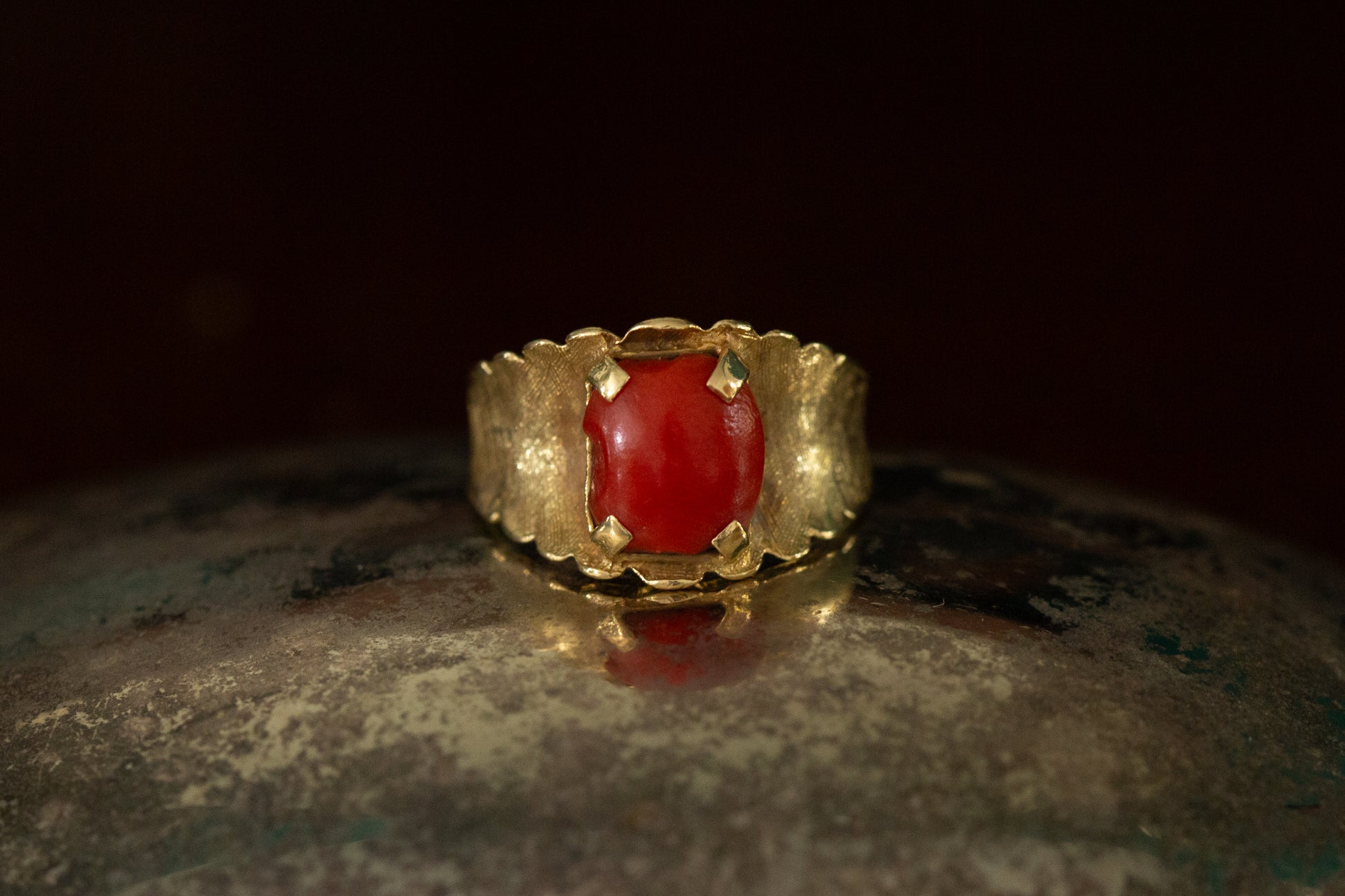 Front view of 18ct yellow gold ring featuring a square-ish red coral cabochon claw set on a wide textured band.