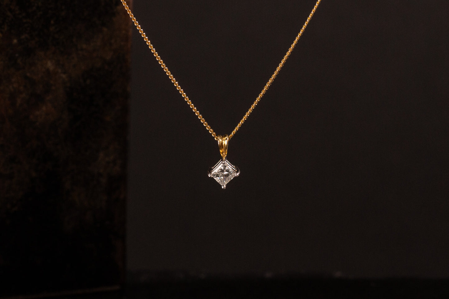 Front view of 18ct gold princess cut diamond solitaire pendant hanging against a dark background.