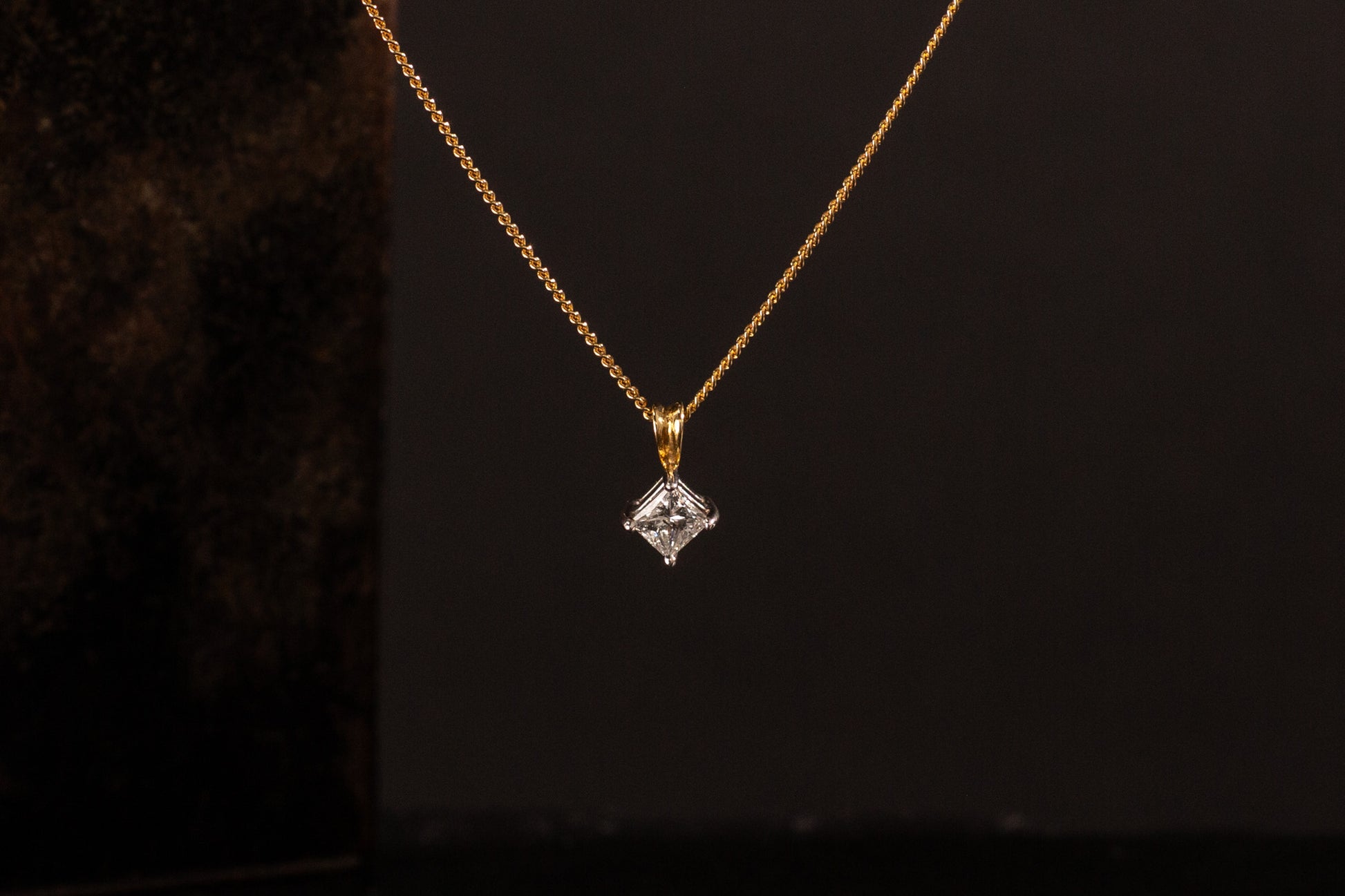 Front view of 18ct gold princess cut diamond solitaire pendant hanging against a dark background.