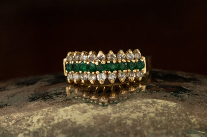 Front view of 9ct yellow gold triple row ring with central emeralds and outer diamond rows claw set on dark prop.
