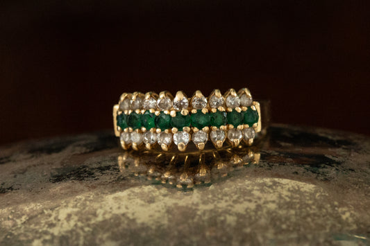 Front view of 9ct yellow gold triple row ring with central emeralds and outer diamond rows claw set on dark prop.