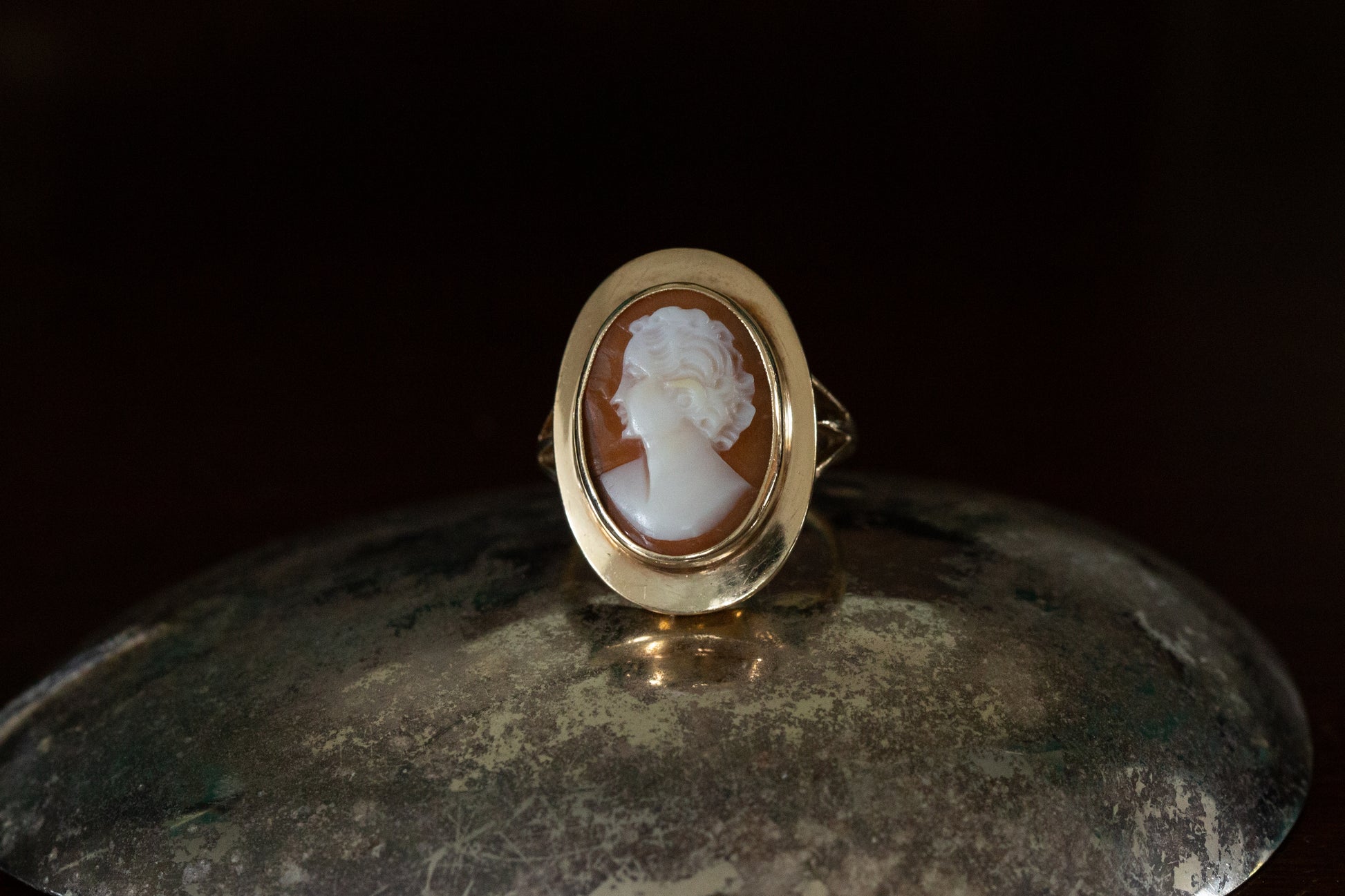 Front view of large oval shell cameo ring depicting a lady's profile rub over set in yellow gold on a dark reflective background.