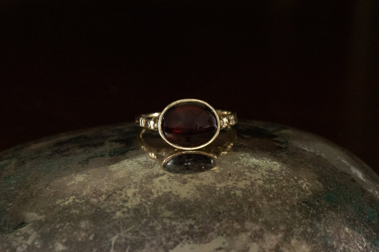 Front view of 9ct yellow gold ring featuring an oval cabochon garnet rub over set on a dark reflective background.