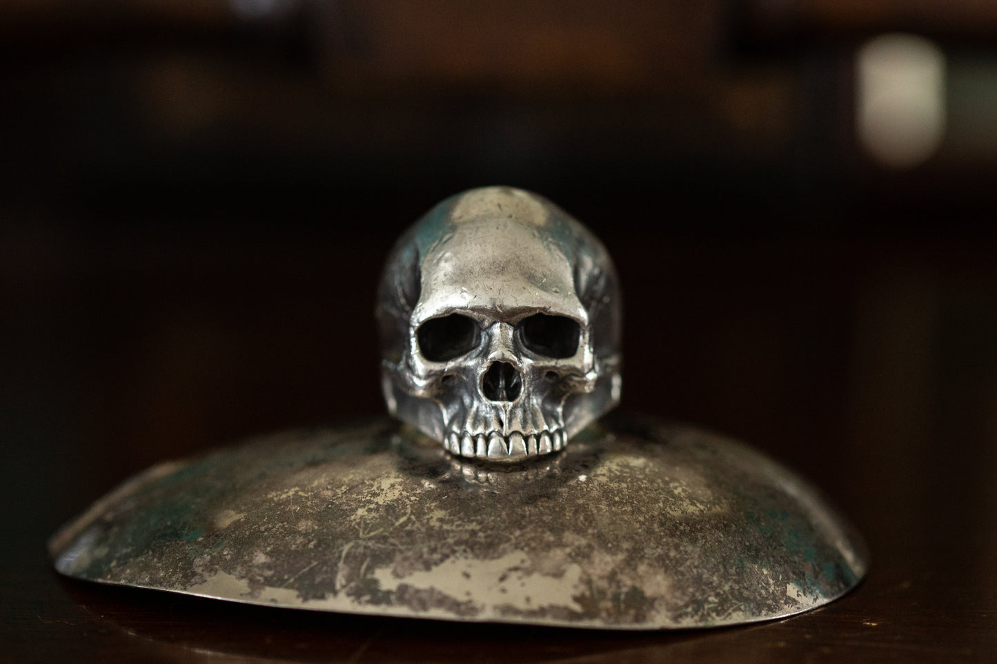 Front view of realistic solid silver skull ring featuring detailed teeth and eye sockets on a dark reflective background.