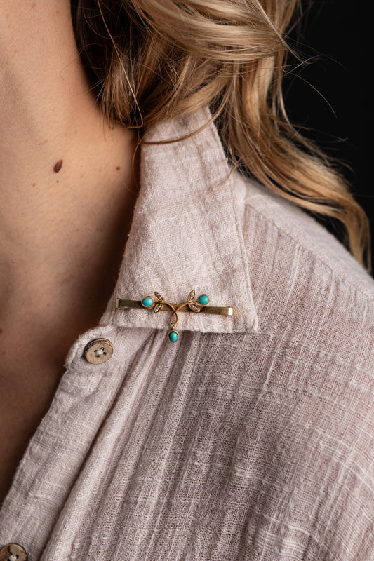 Model wearing Victorian turquoise and pearl bar brooch on the collar of a beige shirt.