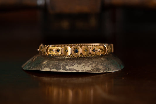 Front view of antique Edwardian gold bangle with star-set sapphires and rose cut diamonds on dark background.