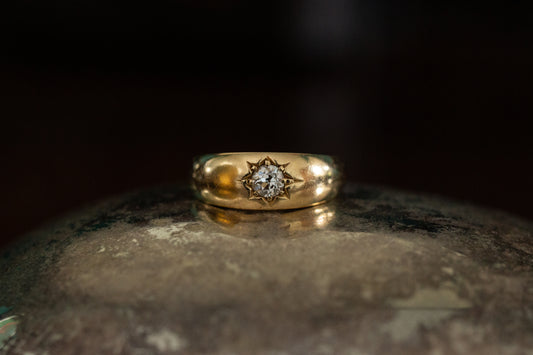 Front view of vintage yellow gold gypsy ring featuring a central star set old cut diamond on a dark reflective background.