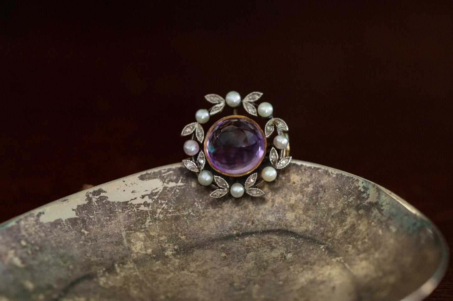 Front view of antique round brooch featuring a central cabochon amethyst surrounded by a wreath of rose cut diamonds and seed pearls in 18ct rose gold.